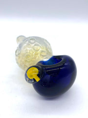Photo of a large fumed spoon pipe with a blue head and a bulbous fumed body that tapers to a small mouthpiece, against a white background. The piece is facing head side right, and a mushroom implosion bubble can be seen on its left side (facing camera).